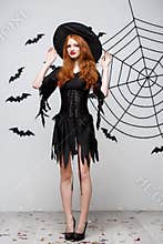 Halloween witch concept - Full-length of Happy Halloween Witch holding posing over dark grey studio background with bat