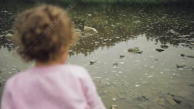 Blonde curly little girl throw stones in the river. Mountains background