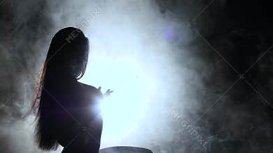 Girl is dancing a sexy dance in the smoke. Black background. Silhouette