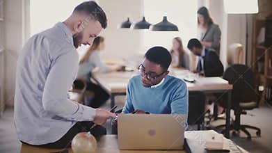 Multiethnic colleagues collaborate in modern trendy office space, look at a document together, coworking in background.