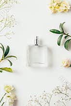 top view of bottle of perfume surrounded with flowers and green branches