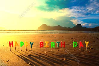 Happy birthday colorful candles on beach sunrise.