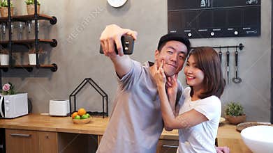 Happy young Asian couple using smartphone for selfie while cooking in the kitchen at home. Man and woman preparing healthy food.