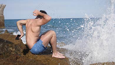 Man with cellphone avoiding it getting wet with wave splash