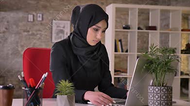 Young beautiful muslim girl in hijab is working with laptop in office, work concept, business concept, communication