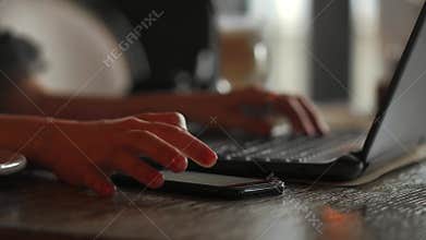 Close-up rear view of young business woman working in office interior on pc holding smartphone and looking at screen