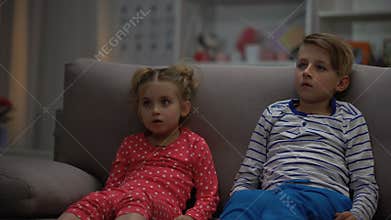 Little boy and girl watching horror movie at night, sitting on sofa, leisure