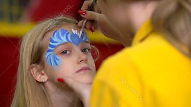 Female painter drawing aqua make-up to pretty child. Close-up motion.