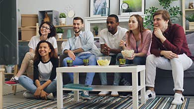Young men and women watching TV laughing eating popcorn in apartment together