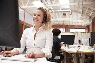 Female Customer Services Agent Working At Desk In Call Center