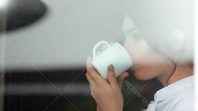 Pensive woman drinking hot beverage dreaming and looking on glass window medium close-up