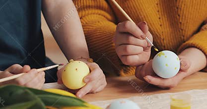 Close up of mother and daughter hands coloring easter eggs with colors and brush. Colorful easter eggs. Preparation of
