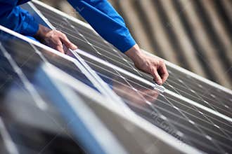 Electrician mounting solar panel on roof of modern house