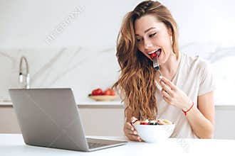 Pretty woman chatting on laptop and eating fruits