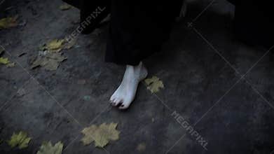 Close up shot of the pale feet of a woman who walks barefoot along the gray park road, a woman dressed in a long dress
