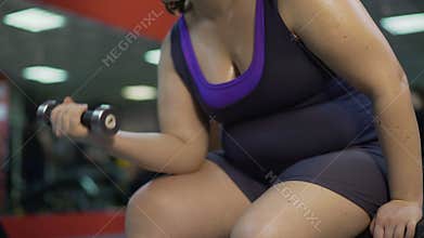 Arms of overweight girl training in gym, doing dumbbell exercise for biceps