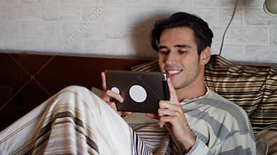 Handsome young man in bed typing on tablet PC