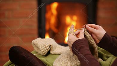 Woman hands knitting wool socks by the fire