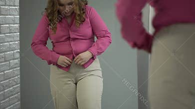 Lady buttoning up her shirt on stomach with great effort, obesity health problem