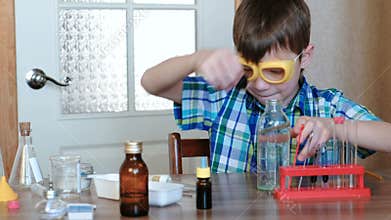 Experiments on chemistry at home. Boy takes a bottle of water and pours water into the tube with a pipette. Front view.