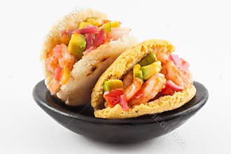 Arepas filled with shrimp ceviche served in a black ceramic dish
