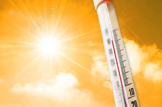 Thermometer against the background of an orange yellow hot glow of clouds and sun, concept of hot weather.