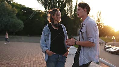 Stylish young man chatting with girlfriend in the park on sunny summer day. Couple in love talking outdoors. Wearing