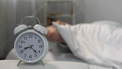 Man in bed waking up to ringing alarm clock, healthy lifestyle, discipline