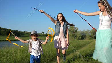 Nice girls with little boy jump with colored ribbons in hand outdoors along lake