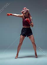 Female fighter trains in boxing bandages in studio on gray background.