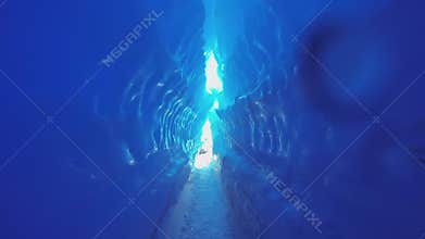 Blue ice cave covered with snow and flooded with light.
