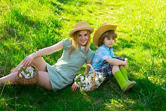 Happy mother at spring day with son picnic. Family mom with kid boy sitting on the grass in park with basket of flower
