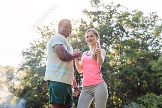 Fitness couple in park with woman giving thumbs-up to camera