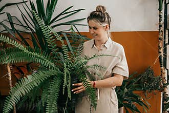 A young woman with smile looks at animated fern in formal small garden of the office space against background of a terracotta wall