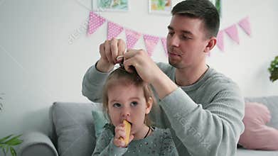 fatherhood, loving caring male parent does his daughter hair and ties her hair up with an elastic band, close-up