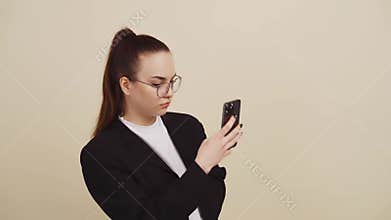 Young woman on beige background works with smartphone and makes selfie.