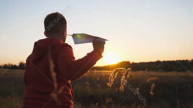 Rear view of cute little child running with a paper airplane through meadow. Carefree small boy jogging along grass