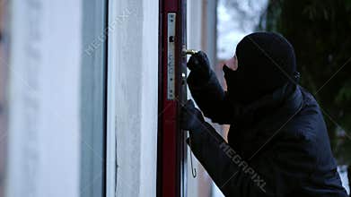Side view thief picking lock entering empty house on winter day. Caucasian young man in ski mask breaking in private