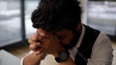 Close-up of frustrated bearded businessman depressed holding head thinking about problems, tapping on forehead, sitting