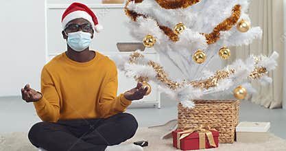 Afro american guy black man wears Christmas hat and medical protective mask feels balance sitting in lotus position on