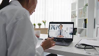 Young Asia lady doctor in white medical uniform using laptop talking video conference call with senior doctor at desk in health