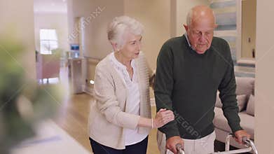 Senior woman helping disabled husband walk at medical clinic