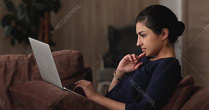 Indian woman sit on comfy sofa working on laptop