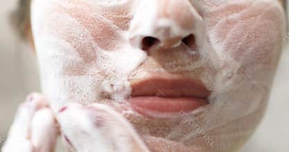Young woman is washing applying foam cleanser on face. Daily facial skincare procedure. Front view