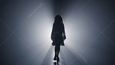Silhouette girl walking darkness. Woman going straight on camera dark background