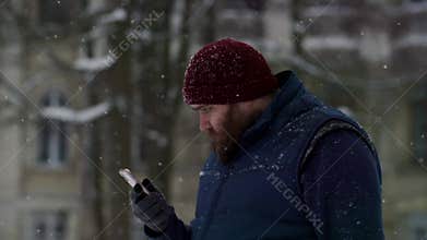 Slo motion man using mobile phone in a snow fall day. A young guy standing alone outdoors and enjoying content in