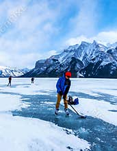Boy enjoys ice hockey on frozen Lake Minnewanka, or Minn-waki (Lake of Spirits), surrounded spectacular mountains.