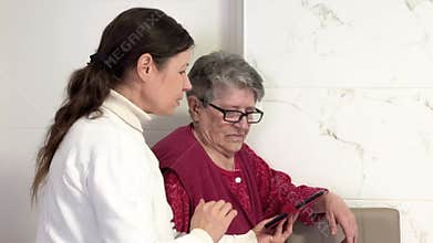 A middle-aged women explains the settings on a cell phone to an elderly grandmother.