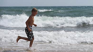 A boy runs along a sandy beach along the surf line against the background of raging sea waves. Live a healthy life.