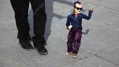 Artist manages puppet which dance on pavement at